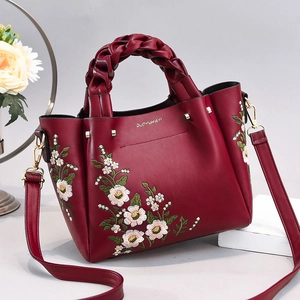 Detailed view of burgundy leather handbag with intricate floral embroidery and woven handle