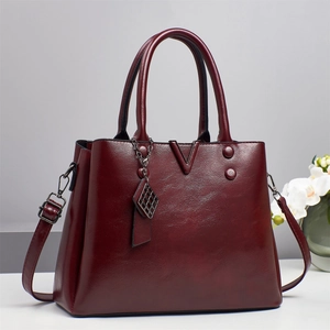 Détail du sac à main en cuir verni bordeaux foncé avec logo V en métal et pompon décoratif