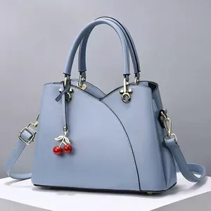 Sac à main bleu pastel avec pendentif cerise et bandoulière sur fond blanc pur