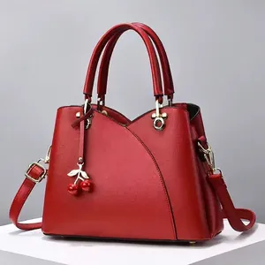 Détail du sac à main en cuir rouge avec coutures incurvées et charm cerise design