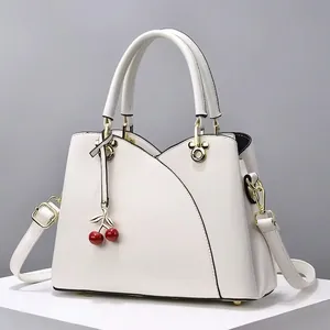 Sac à main blanc en cuir avec liseré noir, fermoir doré et breloque cerise sur un piédestal