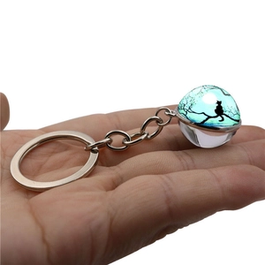 Luminous glass ball keychain with black cat and moon silhouette design held in hand
