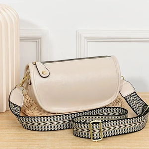 Detail of cream crossbody bag with wide woven strap and gold hardware on woven mat
