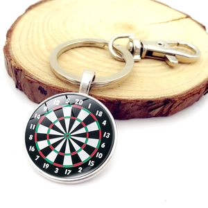 Vintage metal dartboard keychain with glass dome pendant on a natural wood background