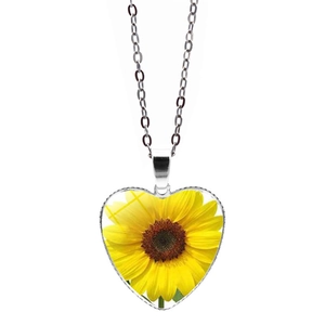 Dettaglio del ciondolo a cuore in vetro con girasole e catena argento su fondo bianco