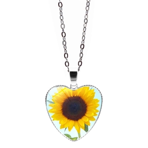 Dettaglio macro del ciondolo a cuore con girasole e catena in metallo argento su bianco