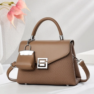 Detail of a brown leather and woven handbag featuring a silver buckle and mini bag charm