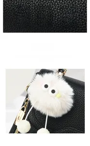Macro detail of a soft white plush monster keychain on a black textured leather handbag