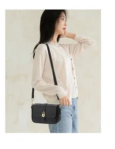 Détail d'un sac bandoulière noir à texture litchi avec un fermoir rotatif doré rond