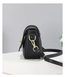Détail d'un sac bandoulière noir en cuir grainé avec ferrures dorées et coutures blanches