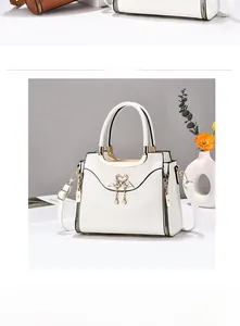 Detail of white leather handbag featuring golden twin swan clasp and pearl tassel charm
