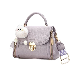 Lavender purple textured leather handbag with wide strap and plush pendant on white background