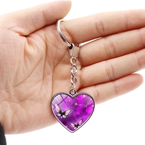 Purple butterfly heart keychain with silver metal frame held in hand over white background
