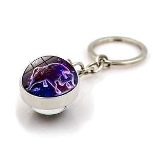 Detail of a silver Taurus zodiac keychain featuring a glowing purple glass ball ornament