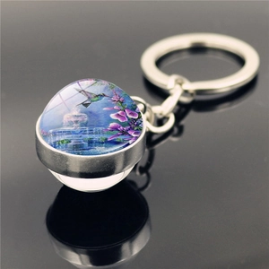 Macro detail of hummingbirds and floral art inside a glass ball keychain pendant