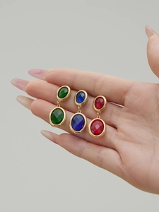 Detail of oval gemstone drop earrings in green, red, and blue with gold-plated finish
