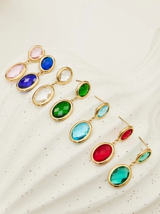 Macro detail of oval gemstones in gold-plated drop earrings displayed on a white tray