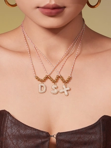 Detail of colorful braided cord necklaces with gold beads and zircon initial pendants