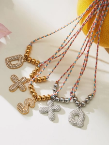 Detailed view of colorful braided necklaces with rhinestone paved letter pendants