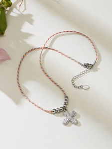 Close-up of tricolor braided rope necklace with stone-set cross and S. Steel logo tag
