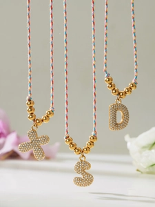 Close-up of gold cubic zirconia letter pendants S and D on colorful braided cords