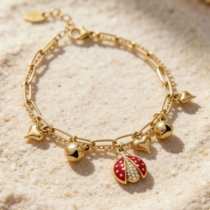 Bracelet à breloques en acier doré avec coccinelle et cloches sur plage de sable blanc
