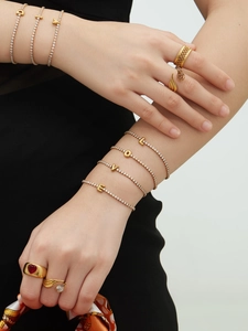 Close-up of gold plated stainless steel letter bracelets and gemstone rings on hands