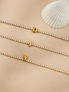Close-up of gold plated tennis bracelets with D-letter, bar, and heart pendants on shell