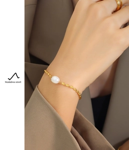 Détail d'un bracelet en acier inoxydable doré avec chaîne à billes olive et une perle blanche