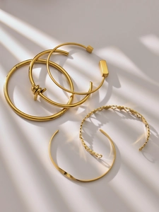 Close-up of 5 gold stainless steel bangles with heart and geometric patterns in soft light