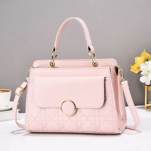 Pink quilted crossbody bag with top handle and golden charm on a minimalist white desk