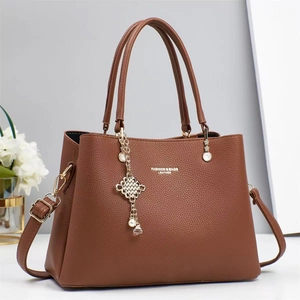 Detail of brown litchi pattern leather handbag with gold lettering and charm