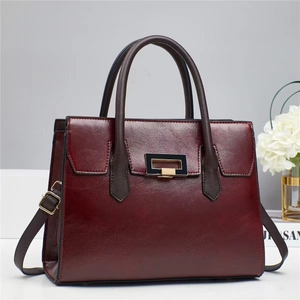 Close-up of deep red leather tote bag featuring gold buckle and brown handles