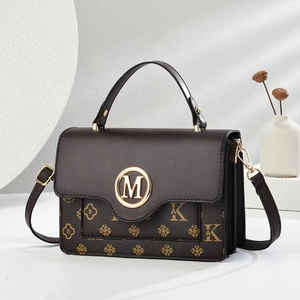 Detalle de bolso marrón con hebilla dorada en forma de M y estampado de logotipos