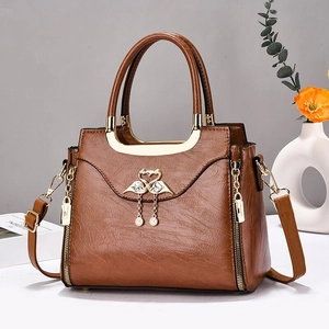 Sac à main marron en cuir avec boucle cygne dorée et bandoulière sur surface blanche