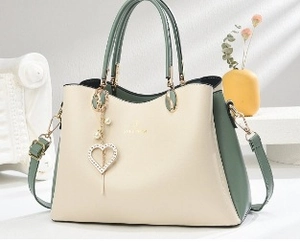 Détail d'un sac à main bicolore crème et vert avec breloque cœur perle et finitions dorées