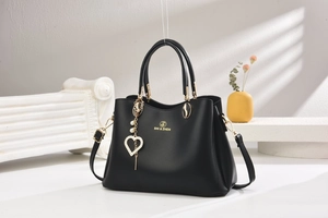 Détail du sac cabas en cuir noir avec logo doré et pendentif cœur en perles