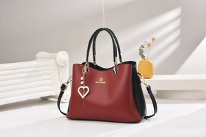 Détail du sac en cuir rouge et noir avec logo doré et breloque perle en cœur