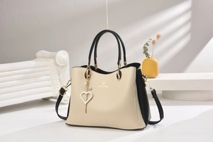 Détail du sac cabas beige et noir avec logo doré et pendentif en forme de cœur perlé