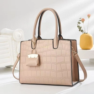 Elegant beige stone-patterned handbag with mini charm and gold hardware on a minimalist desk