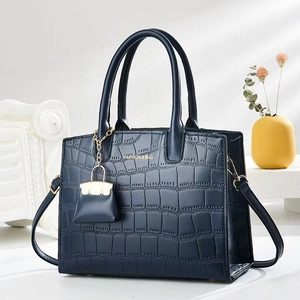 Detail of dark blue faux crocodile leather handbag with mini bag charm and gold embossing