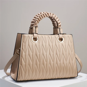 Sac fourre-tout beige avec matelassage plissé en V et poignée tissée sur socle blanc
