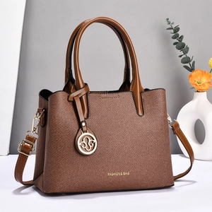 Sac fourre-tout tissé marron avec détails dorés et bandoulière sur fond gris minimaliste