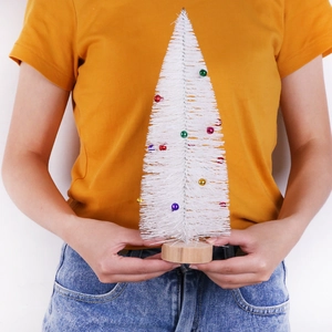 Detailed view of small white Christmas tree with colorful baubles held by hand