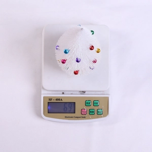 Mini white tabletop Christmas tree with colorful ornaments on a digital scale weighing 69g