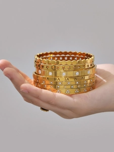 Close-up of gold stainless steel bangle set featuring Roman numerals and zircon stones