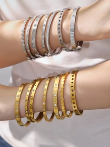 Detail of stacked gold and silver bangles with Roman numerals and star motifs on wrist