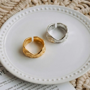 Minimalist irregular wavy open rings in gold and silver finish on a ceramic plate