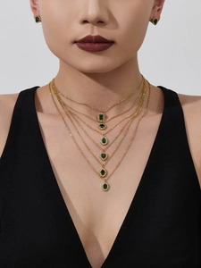 Detail of layered gold necklaces and green gemstone earrings worn by model