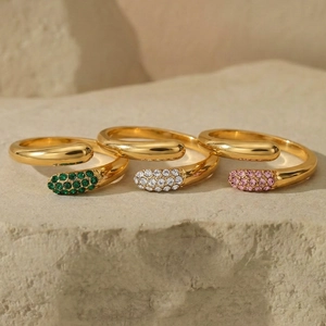 Three gold teardrop rings with green white and pink zircon stones on stone background